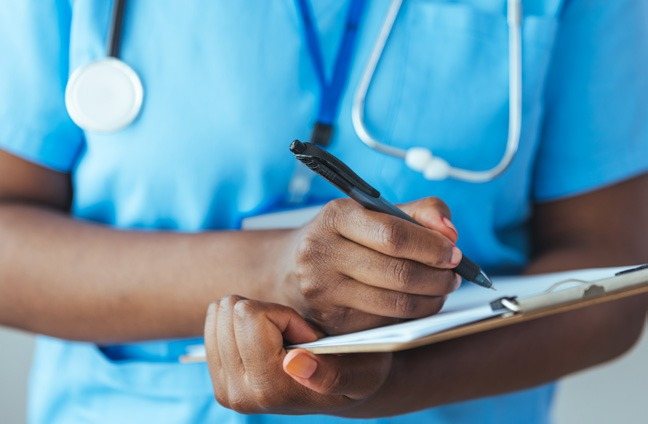 A nurse in scrubs writing notes on a clipboard