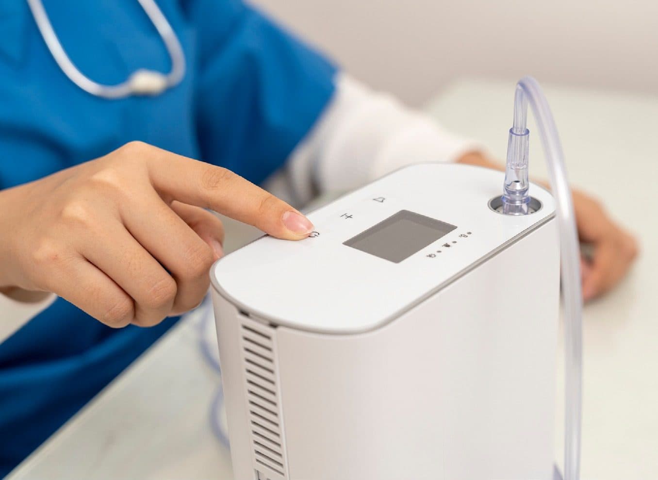 A clinician's hand on the controls of a portable oxygen concentrator